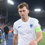Een KRC Genk-speler in wit wedstrijdshirt loopt na een wedstrijd over het veld.