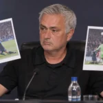 Een trainer houdt tijdens een persconferentie uitgeprinte wedstrijdfoto's omhoog.
