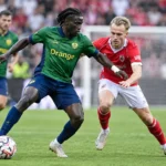 Voetballers in groen-blauwe en rode tenues tijdens een duel om de bal.