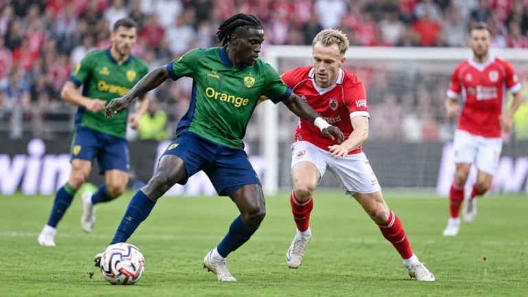 Voetballers in groen-blauwe en rode tenues tijdens een duel om de bal.