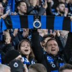 Een collectieve groep Club Brugge-supporters met één blauw-zwarte sjaal in de tribune.