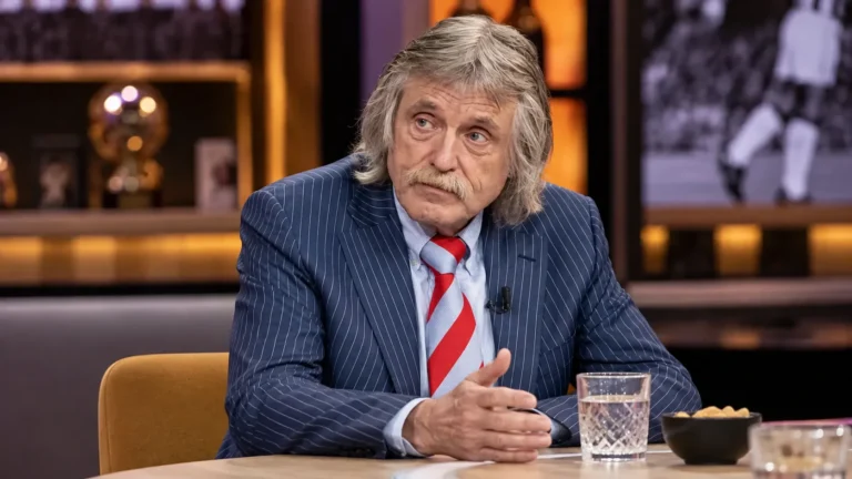 Johan Derksen aan een talkshowtafel in een televisiestudio.