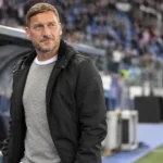 Francesco Totti staat rustig naast de dug-out in een voetbalstadion.