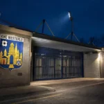 De verlichte ingang van Het Kuipje met een KVC Westerlo-embleem aan de gevel.