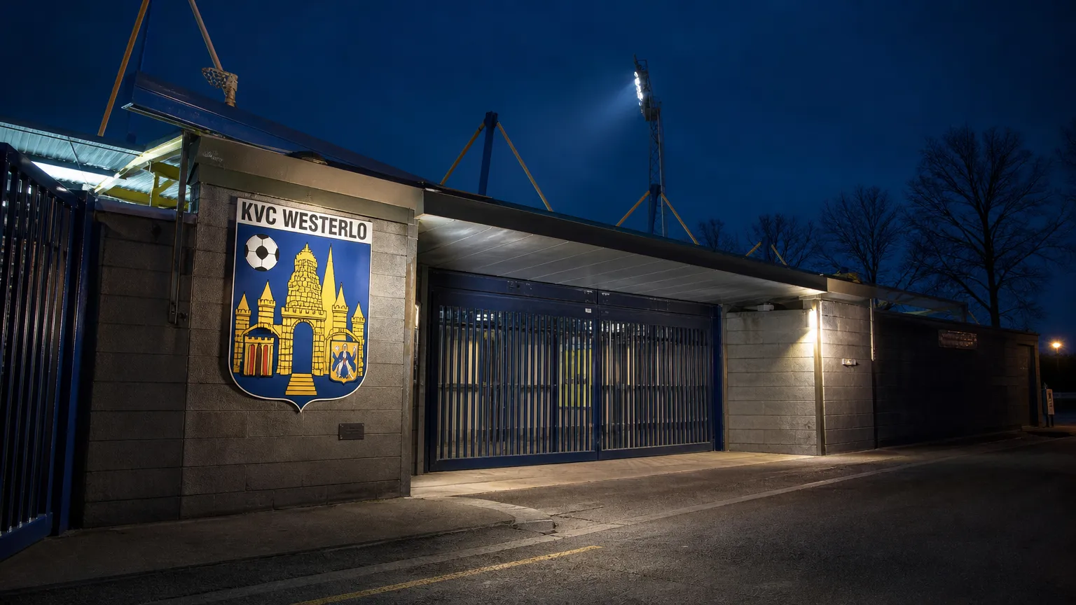 De verlichte ingang van Het Kuipje met een KVC Westerlo-embleem aan de gevel.