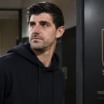 Thibaut Courtois in een donkere hoodie naast een vast bord van de Belgische voetbalbond.