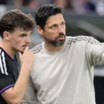 Een coach en een speler van Anderlecht staan samen langs het veld tijdens een nieuw voetbalmoment.