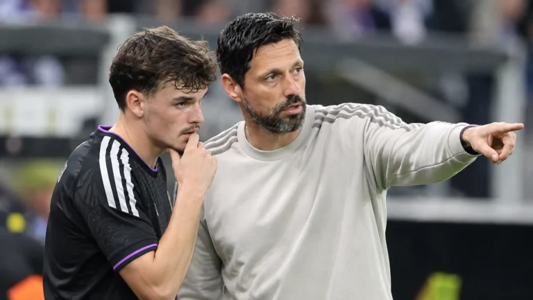 Een coach en een speler van Anderlecht staan samen langs het veld tijdens een nieuw voetbalmoment.