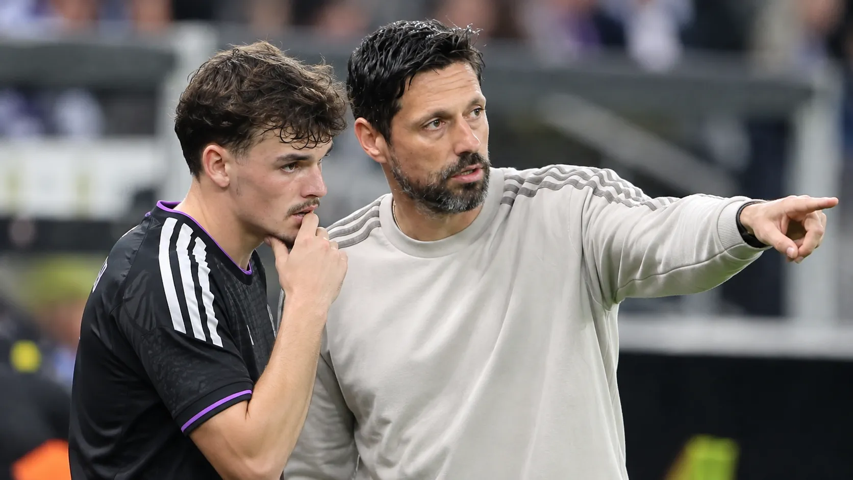 Een coach en een speler van Anderlecht staan samen langs het veld tijdens een nieuw voetbalmoment.