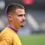 Leander Dendoncker in gele spelerskleding langs een voetbalveld.