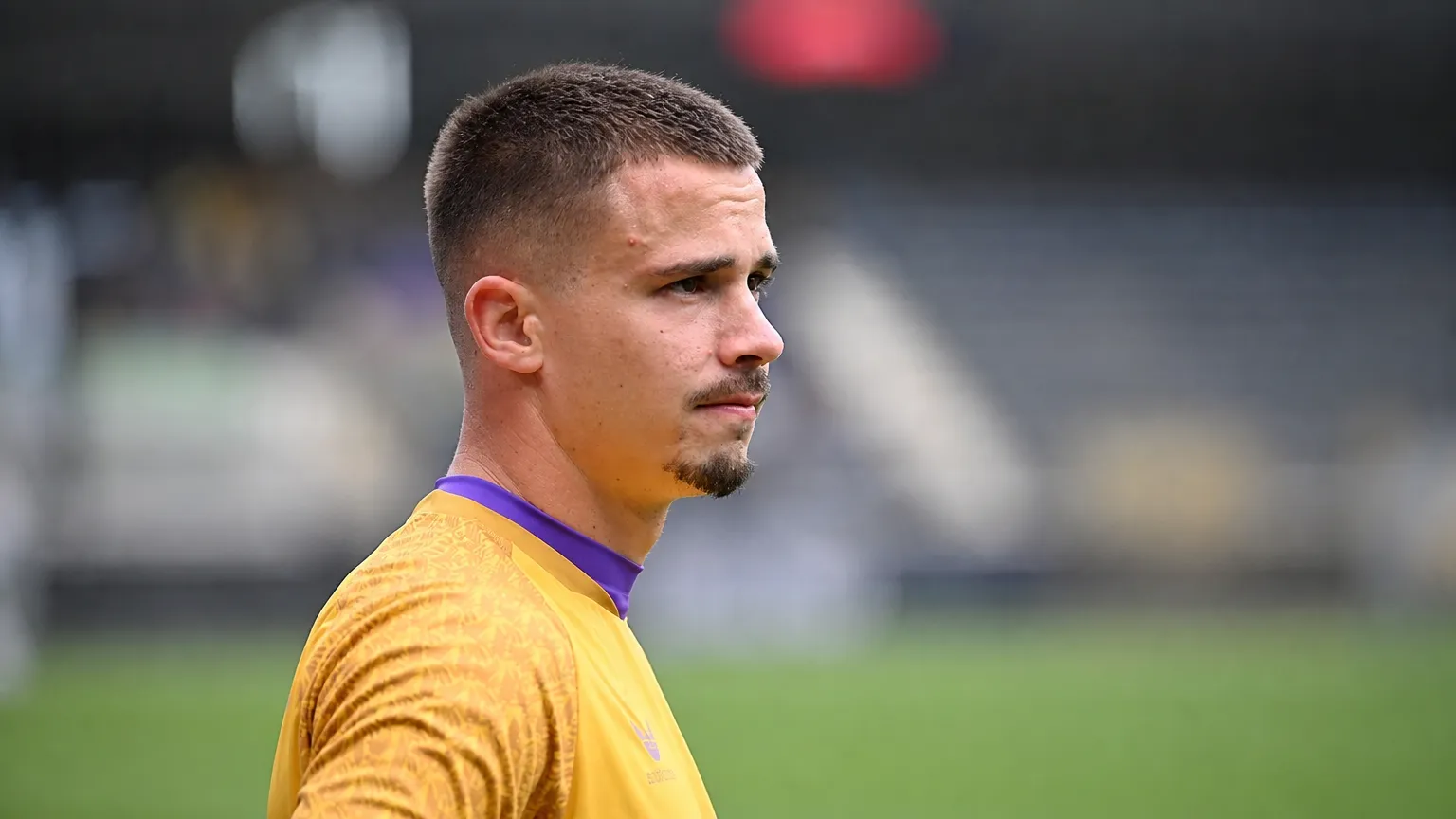 Leander Dendoncker in gele spelerskleding langs een voetbalveld.