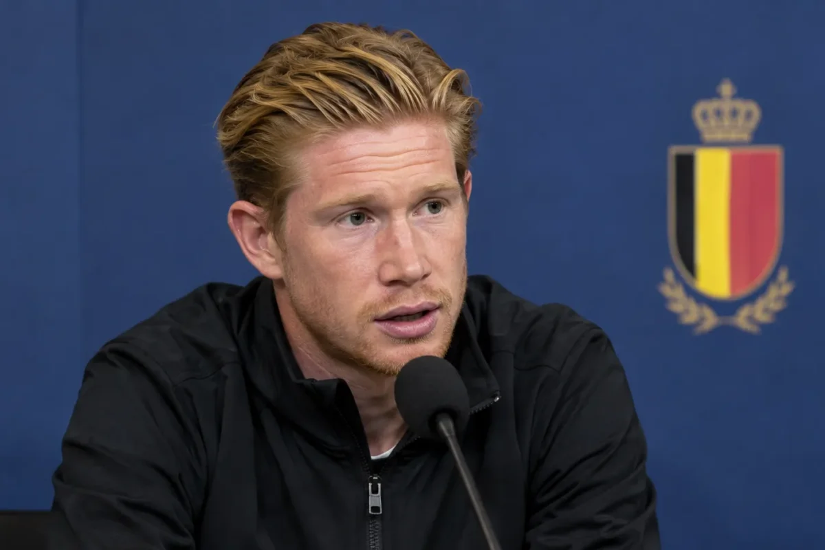 Kevin De Bruyne spreekt in een mediazone in een donkere trainingsjas voor een microfoon.
