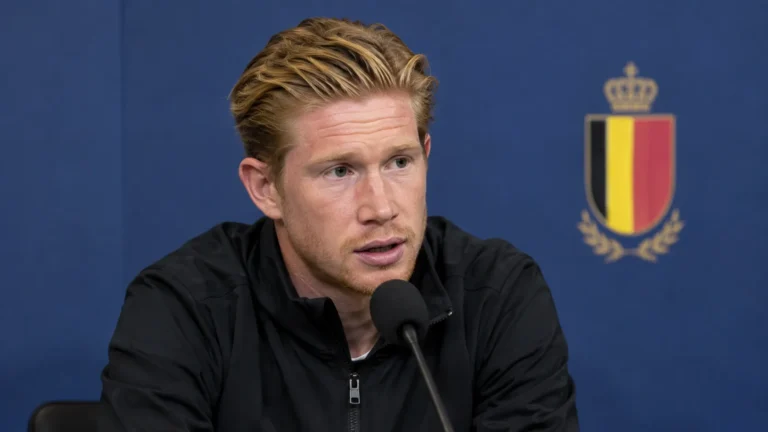 Kevin De Bruyne spreekt in een mediazone in een donkere trainingsjas voor een microfoon.