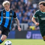 Twee voetballers in verschillende clubtenues tijdens wedstrijdactie.