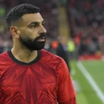 Mohamed Salah in een rood voetbalshirt langs de rand van een stadionveld.