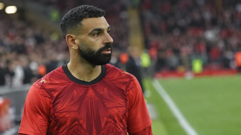 Mohamed Salah in een rood voetbalshirt langs de rand van een stadionveld.