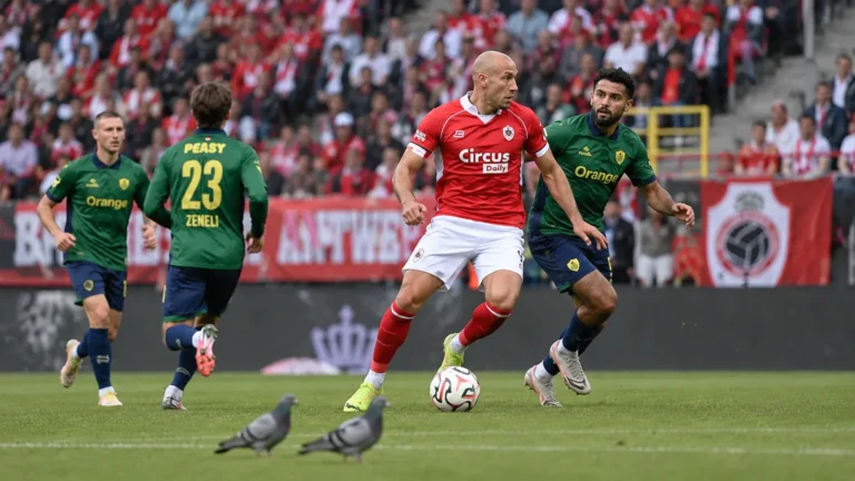 Twee duiven op het gras terwijl spelers van Antwerp en Union verder spelen.