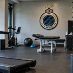 Lege revalidatieruimte van Club Brugge met trainingsmateriaal en een clubembleem aan de muur.
