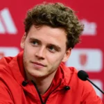 Maxim De Cuyper tijdens een media-interview in een rode persruimte.