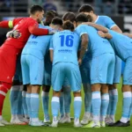 Spelers van KAA Gent verzamelen in een hechte kring op het veld.