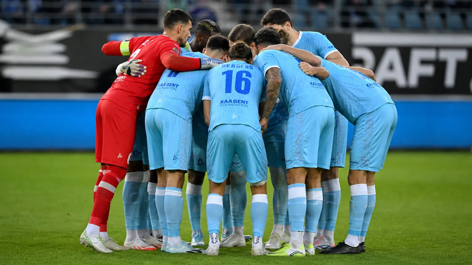 Spelers van KAA Gent verzamelen in een hechte kring op het veld.