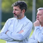 Twee leden van de Belgische technische staf volgen een training langs het veld.