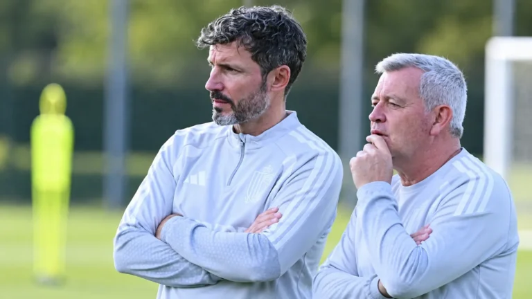 Twee leden van de Belgische technische staf volgen een training langs het veld.