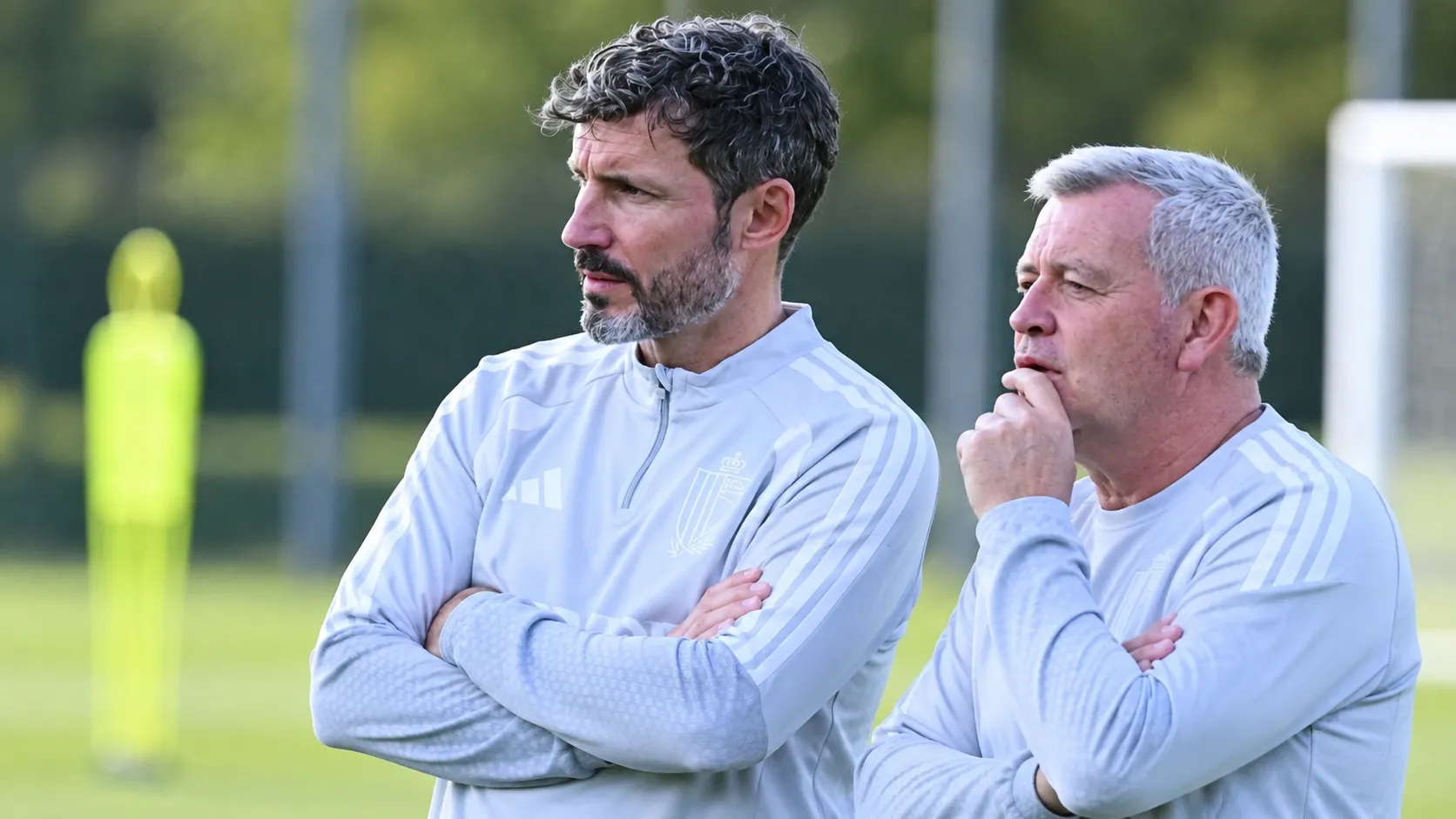 Twee leden van de Belgische technische staf volgen een training langs het veld.