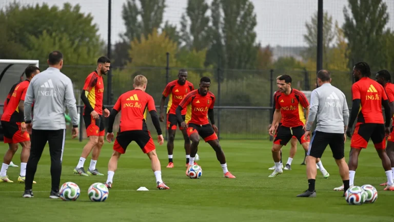 Een groep spelers en stafleden in rode trainingskleding tijdens een oefensessie op een trainingsveld.
