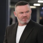 Wayne Rooney in een zwarte blazer in een neutrale mixed zone van een voetbalstadion.