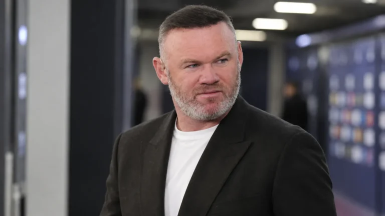 Wayne Rooney in een zwarte blazer in een neutrale mixed zone van een voetbalstadion.