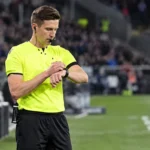 Daniel Siebert controleert zijn horloge naast het voetbalveld in scheidsrechterstenue.