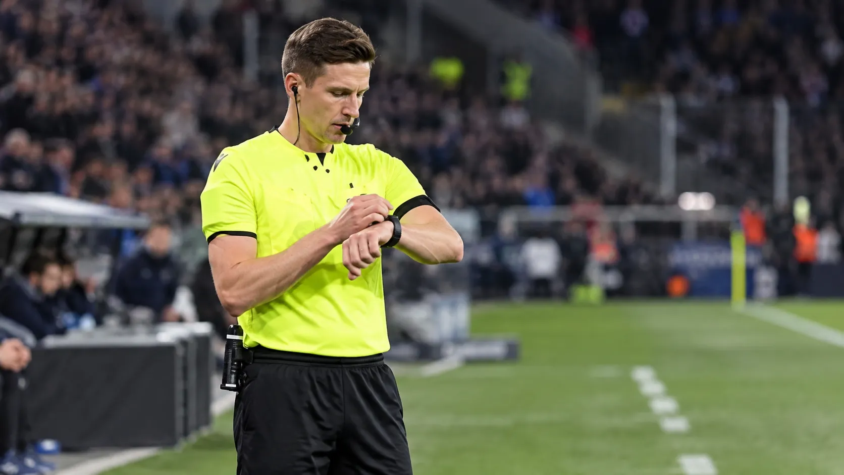 Daniel Siebert controleert zijn horloge naast het voetbalveld in scheidsrechterstenue.
