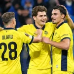 Drie voetballers in gele shirts vieren samen tijdens een wedstrijd.