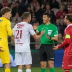 Voetballers verzamelen zich rond een scheidsrechter na een rode kaart.