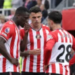 Drie Sunderland-spelers in rood-wit gestreepte shirts overleggen aan de rand van het veld.