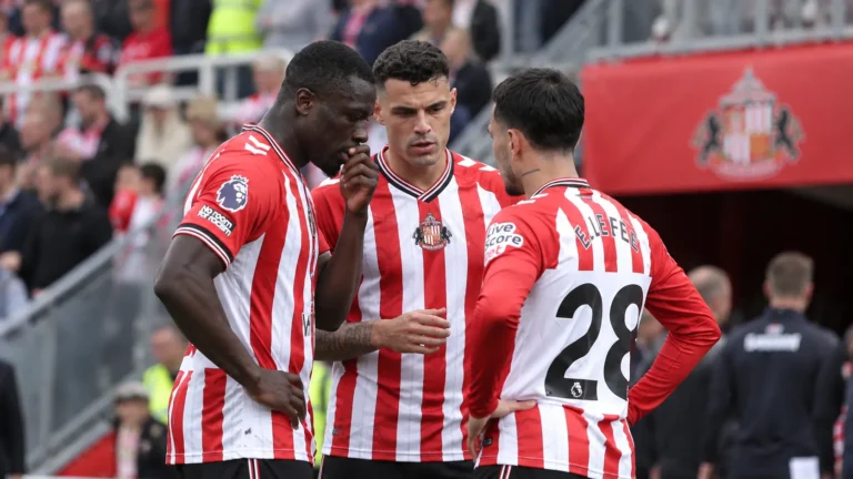 Drie Sunderland-spelers in rood-wit gestreepte shirts overleggen aan de rand van het veld.