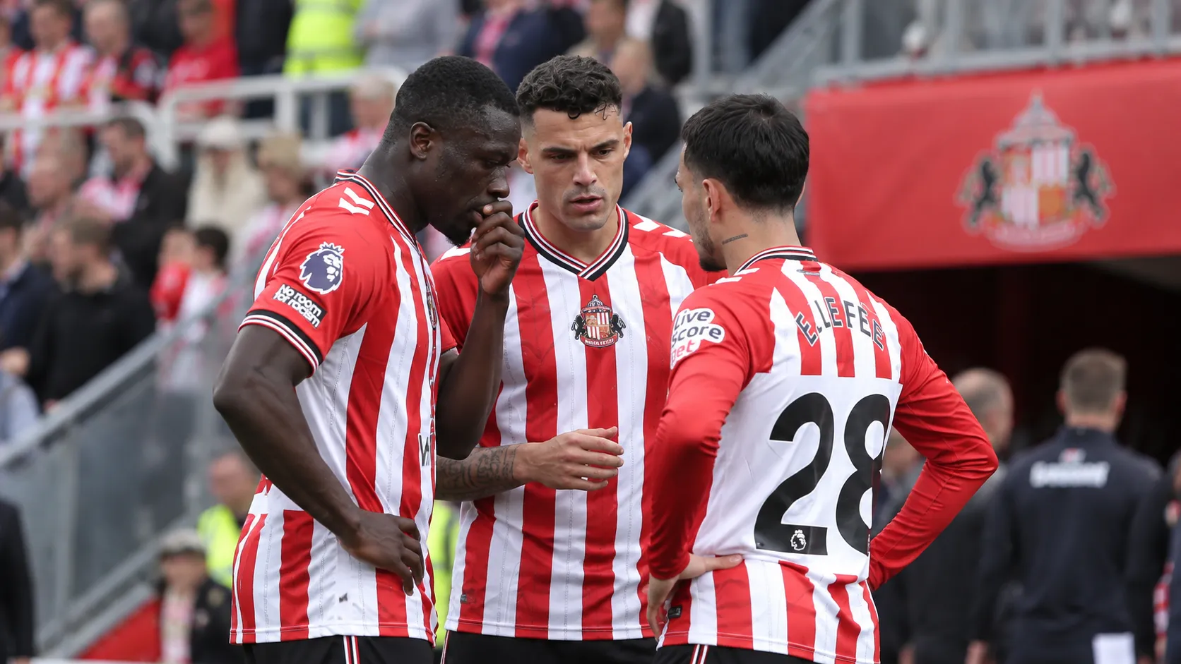 Drie Sunderland-spelers in rood-wit gestreepte shirts overleggen aan de rand van het veld.