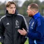 Een jonge speler en een staflid van de Belgische U21 overleggen langs de zijlijn.