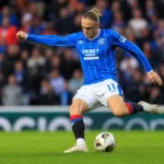 Thelo Aasgaard haalt uit vanop afstand in een blauw gestreept voetbalshirt.