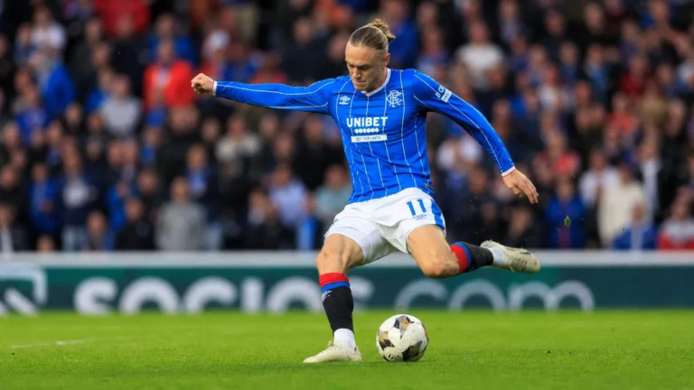 Thelo Aasgaard haalt uit vanop afstand in een blauw gestreept voetbalshirt.