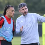 Een bondscoach geeft tijdens een training aanwijzingen aan een speler in trainingskleding.