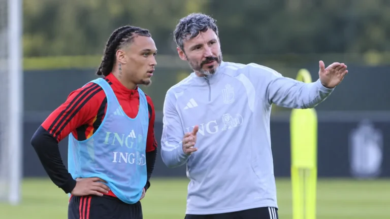 Een bondscoach geeft tijdens een training aanwijzingen aan een speler in trainingskleding.