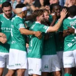 Een groep Lommel-spelers viert samen naast het veld in groene wedstrijdtenues.