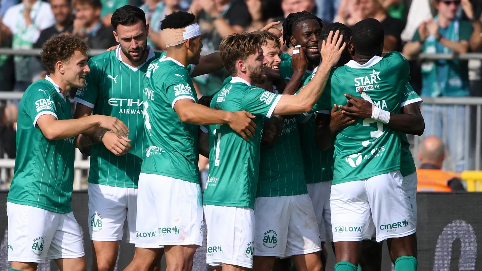 Een groep Lommel-spelers viert samen naast het veld in groene wedstrijdtenues.