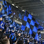 Club Brugge-supporters zwaaien met blauw-zwarte vlaggen in de tribune.