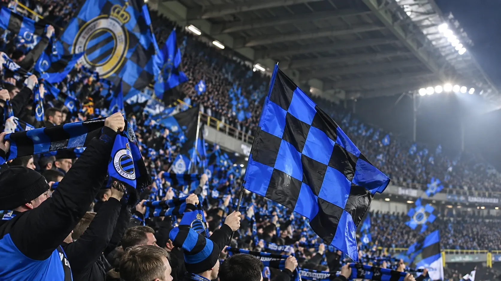 Club Brugge-supporters zwaaien met blauw-zwarte vlaggen in de tribune.