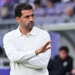 Mo Messoudi staat in een wit poloshirt langs de zijlijn van een stadion.