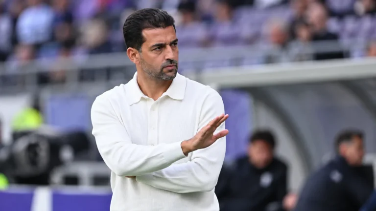 Mo Messoudi staat in een wit poloshirt langs de zijlijn van een stadion.