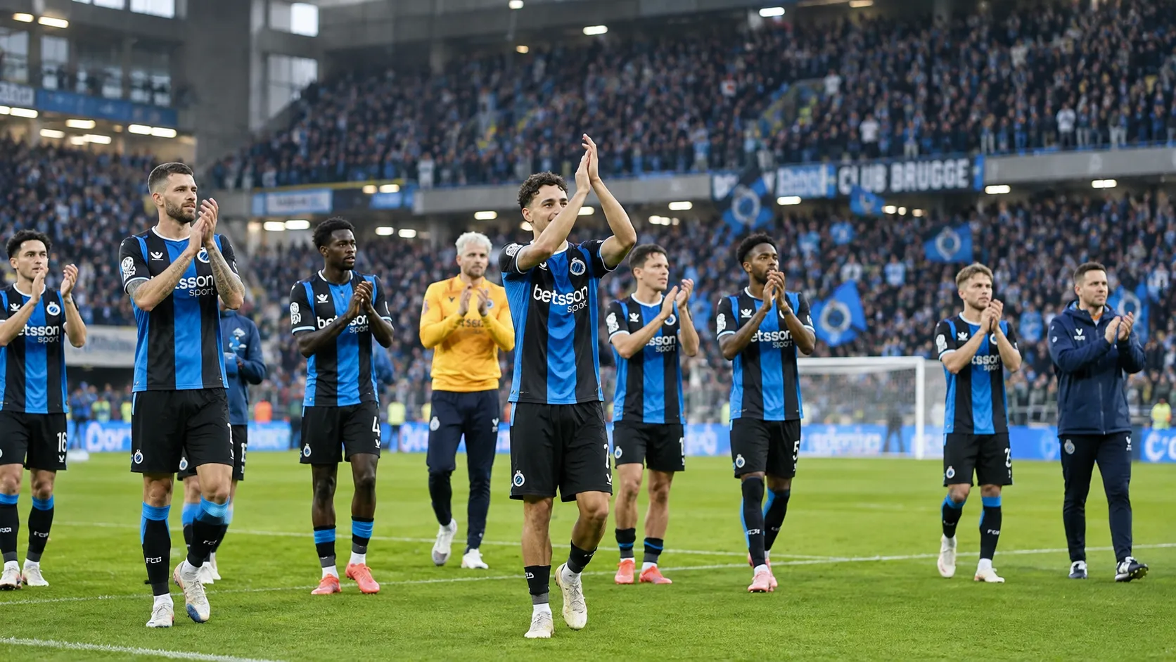 Een groep spelers van Club Brugge applaudisseert op het veld voor de tribune.